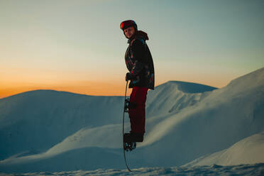 Ein Mann im Skianzug, mit Helm und Skibrille auf einem verschneiten Bergkamm bei Sonnenuntergang - CUF55343
