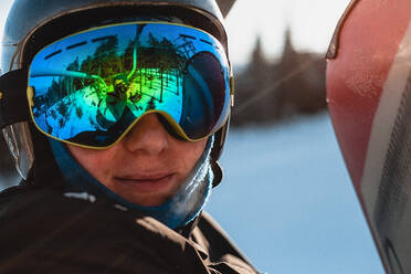 Kopf und Schultern einer Person mit schwarzem Helm und dunkler Schutzbrille auf einer Skipiste. - CUF55365