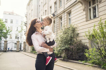 A mother holding her daughter and giving her a kiss in a street setting in Berlin. - CUF55374