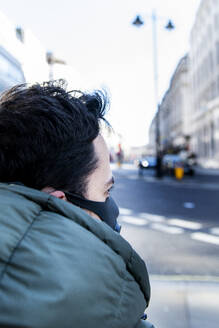 View down a London street over the shoulder of a man wearing a face mask. - CUF55377