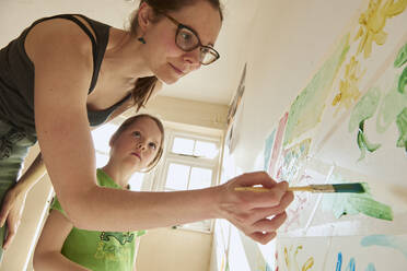 Smiling woman and girl indoors during Corona virus crisis, painting on a wall. - CUF55386