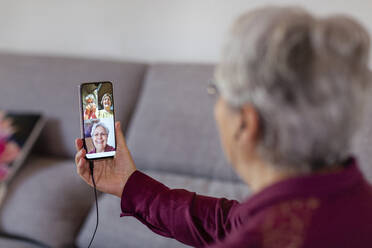 A woman holding up a mobile phone and looking at three friends on screen during social isolation, skype or whatsapp party. - CUF55433