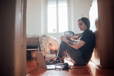 Woman sitting on bedroom floor with laptop computer during Corona virus crisis. - CUF55456