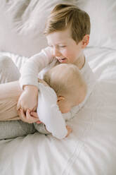 Toddler boy and baby sister playing on bed at home - CAVF81109