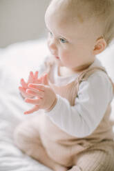 Baby-Mädchen klatscht Hände auf Bett in weichem Licht - CAVF81111