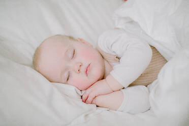 Baby-Mädchen schläft friedlich in weißen Bett mit Blick auf die Kamera mit den Händen für - CAVF81113