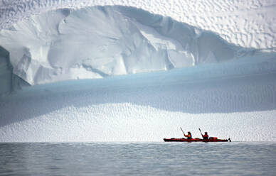 Two men rowing their sea kayak along an iceberg in Greenland - CAVF81235
