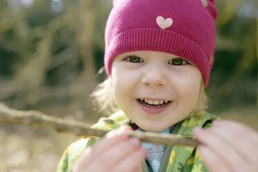 Porträt eines lächelnden kleinen Mädchens mit Zweig in der Natur - BRF01441