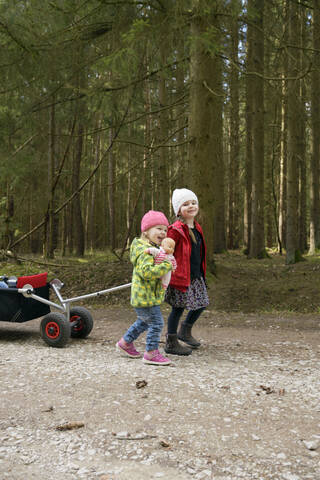 Zwei kleine Schwestern ziehen eine Draisine auf einem Waldweg, lizenzfreies Stockfoto