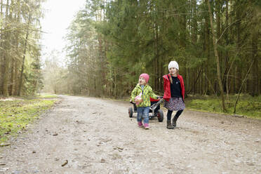 Two little sisters pulling trolley on forest track - BRF01454