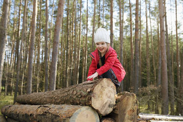 Porträt eines glücklichen kleinen Mädchens, das auf einen Holzstapel im Wald klettert - BRF01459