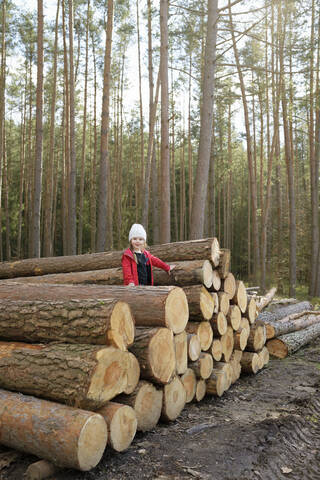 Lächelndes kleines Mädchen steht auf einem Holzstapel im Wald, lizenzfreies Stockfoto