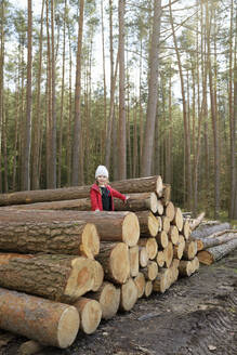 Lächelndes kleines Mädchen steht auf einem Holzstapel im Wald - BRF01463