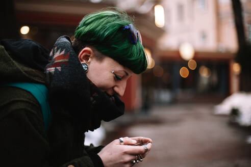 Porträt einer glücklichen nicht-binären Hipster-Frau, die ein Smartphone in der Stadt benutzt - CAVF81364