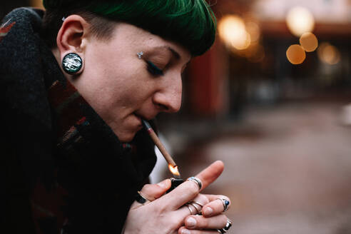 Porträt einer nicht-binären Hipster-Frau, die sich in der Stadt eine Zigarette anzündet - CAVF81366
