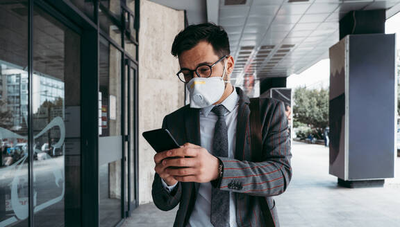Business man with protective face mask using phone on city street. - CAVF81373