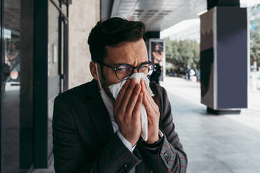 Sick man with protective face mask coughing and sneezing on street. - CAVF81374