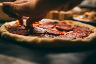 Nahaufnahme der Hand eines Bäckers in weißer Uniform beim Pizzabacken in der Küche - CAVF81396