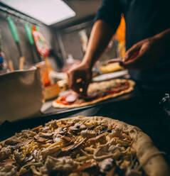 Nahaufnahme der Hand eines Bäckers in weißer Uniform beim Pizzabacken in der Küche - CAVF81400