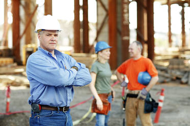 Porträt eines männlichen Bauführers mit zwei Arbeitern dahinter - CAVF81423