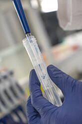 The lab technician performs the experiment by injecting the blue liquid into a test tube - CAVF81442