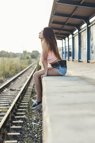 Nachdenkliche junge Frau sitzt an der Bahnsteigkante, lizenzfreies Stockfoto