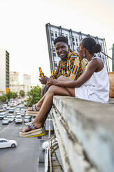 Paar sitzt auf einer Dachterrasse in der Stadt und trinkt Bier, Maputo, Mosambik - VEGF02264