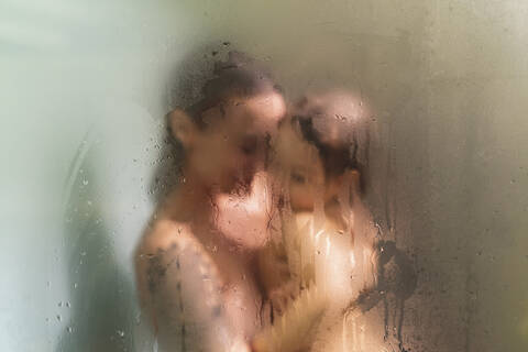 Daughter in mother's arms in the shower behind wet glass stock photo