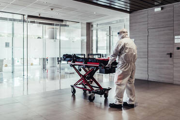 Krankenwagen, Arzt im Schutzanzug schiebt leere Bahre - JAF00002