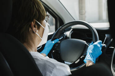 Frau mit Maske und Handschuhen fährt Auto - XLGF00174