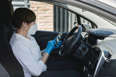 Frau mit Maske im Auto benutzt Smartphone - XLGF00175