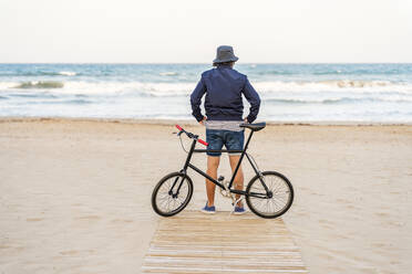 Erwachsener Mann mit Fahrrad, der am Strand steht und das Meer beobachtet - DLTSF00683