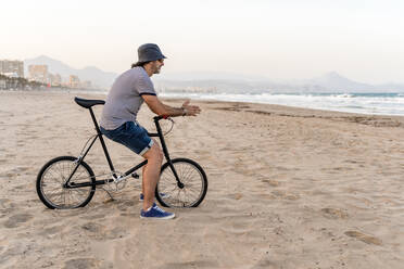 Erwachsener Mann mit Fahrrad, der am Strand sitzt und das Meer beobachtet - DLTSF00688