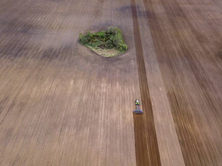 Russland, Region Moskau, Luftaufnahme eines Traktors auf einem landwirtschaftlichen Feld mit Bäumen - KNTF04610