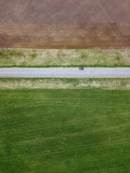 Russia, Moscow Oblast, Aerial view of car driving along country road stretching between brown and green fields - KNTF04629