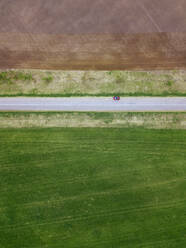 Russland, Moskauer Gebiet, Luftaufnahme eines Autos auf einer Landstraße, die sich zwischen braunen und grünen Feldern erstreckt - KNTF04629