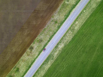 Russia, Moscow Oblast, Aerial view of car driving along country road stretching between brown and green fields - KNTF04631