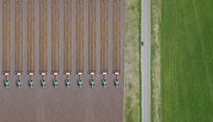 Russia, Aerial view of row of tractors plowing brown field - KNTF04635