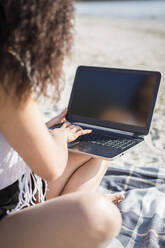 Crop Ansicht der jungen Frau sitzt auf einer Decke am Strand mit Laptop - ASCF01355