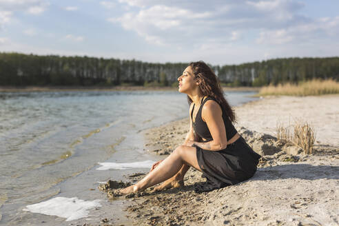 Junge Frau sitzt am Seeufer und genießt das Sonnenlicht - ASCF01364