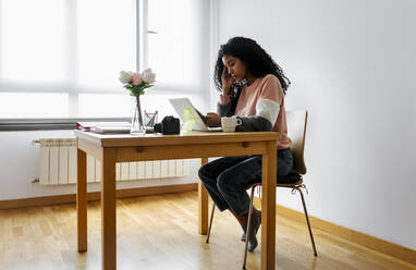 Junge Frau arbeitet von zu Hause aus mit Laptop und Smartphone - MGOF04303