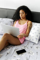 Beautiful young woman lying in bed at home using laptop - MGOF04311