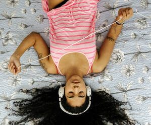 Top view of beautiful young woman lying on bed at home listening to music - MGOF04318