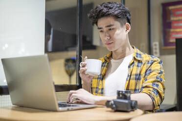 Porträt eines jungen Touristen mit einer Tasse Kaffee in einer Herberge und einem Laptop - JCZF00069