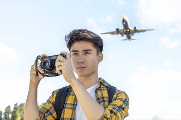 Porträt eines jungen Touristen mit Kamera und Flugzeug über ihm - JCZF00075