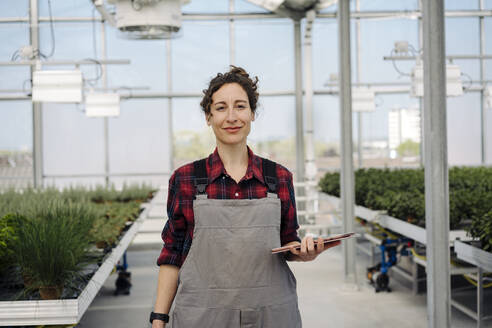 Portrait of confident woman holding tablet in greenhouse of a gardening shop - JOSEF00659