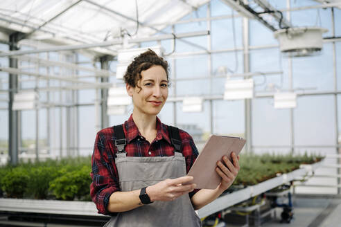 Portrait of confident woman holding tablet in greenhouse of a gardening shop - JOSEF00663