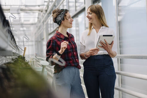 Smiling gardener and businesswoman with tablet in greenhouse of a gardening shop - JOSEF00696