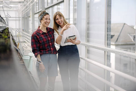 Happy gardener and businesswoman with tablet in greenhouse of a gardening shop stock photo