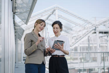 Two businesswomen with tablet and wind turbine model having a meeting at a greenhouse - JOSEF00709